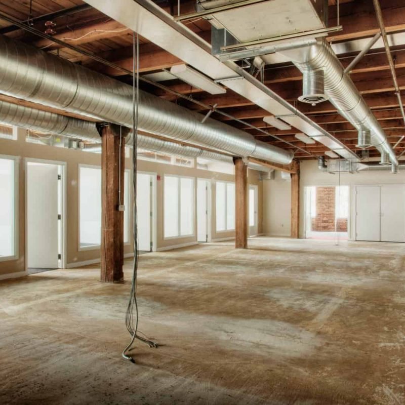 Spacious commercial interior under renovation with exposed ductwork and large windows.