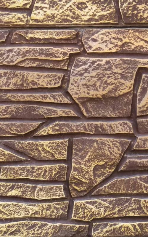 Close-up of textured stone wall with green ivy on the side.